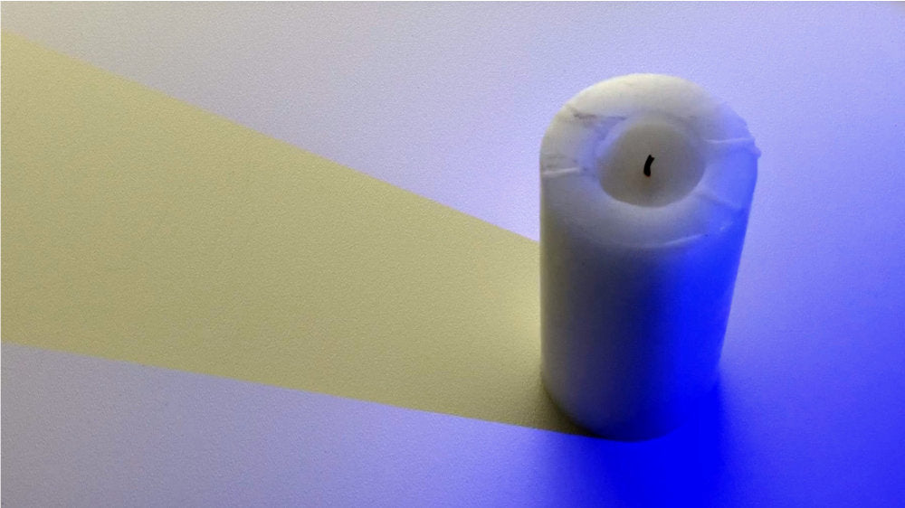 Candle with a blue light on it casting a yellow shadow 